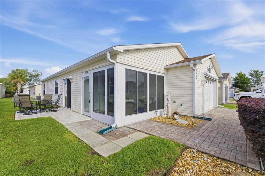 A light-colored house features a screened-in porch, a paved patio, and a grassy yard — 1714 EL NINO STREET, THE VILLAGES, FL