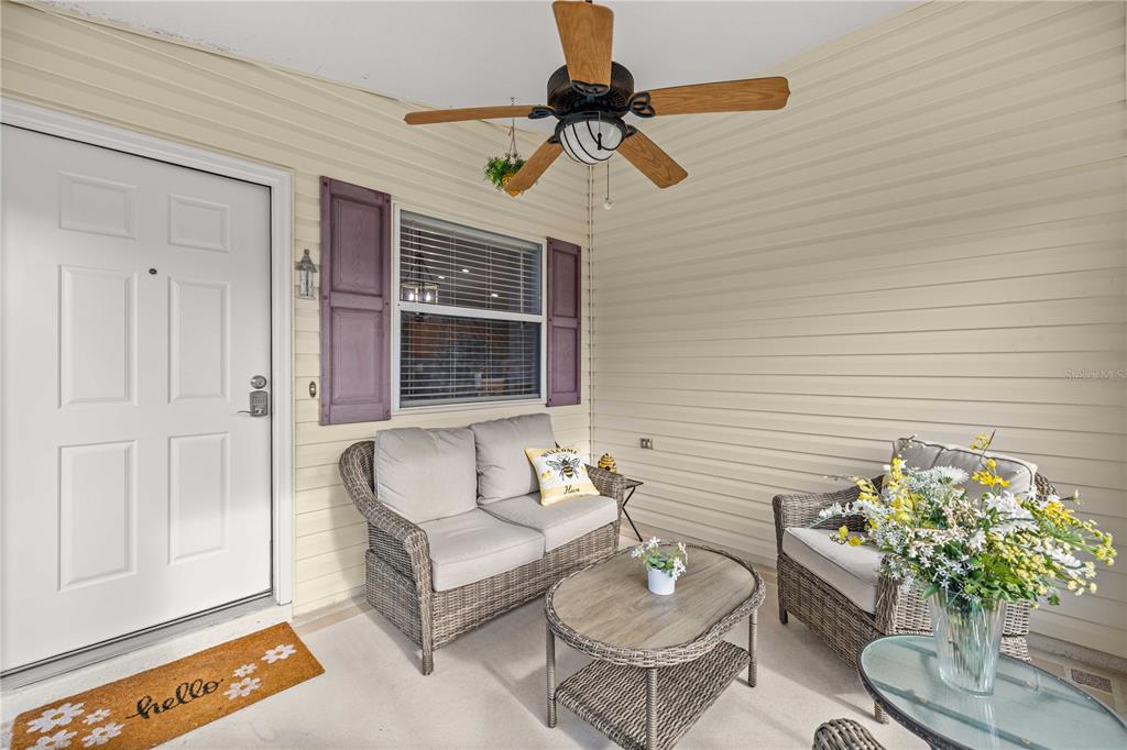 A covered porch features wicker furniture, a ceiling fan, and a white front door — 1714 EL NINO STREET, THE VILLAGES, FL