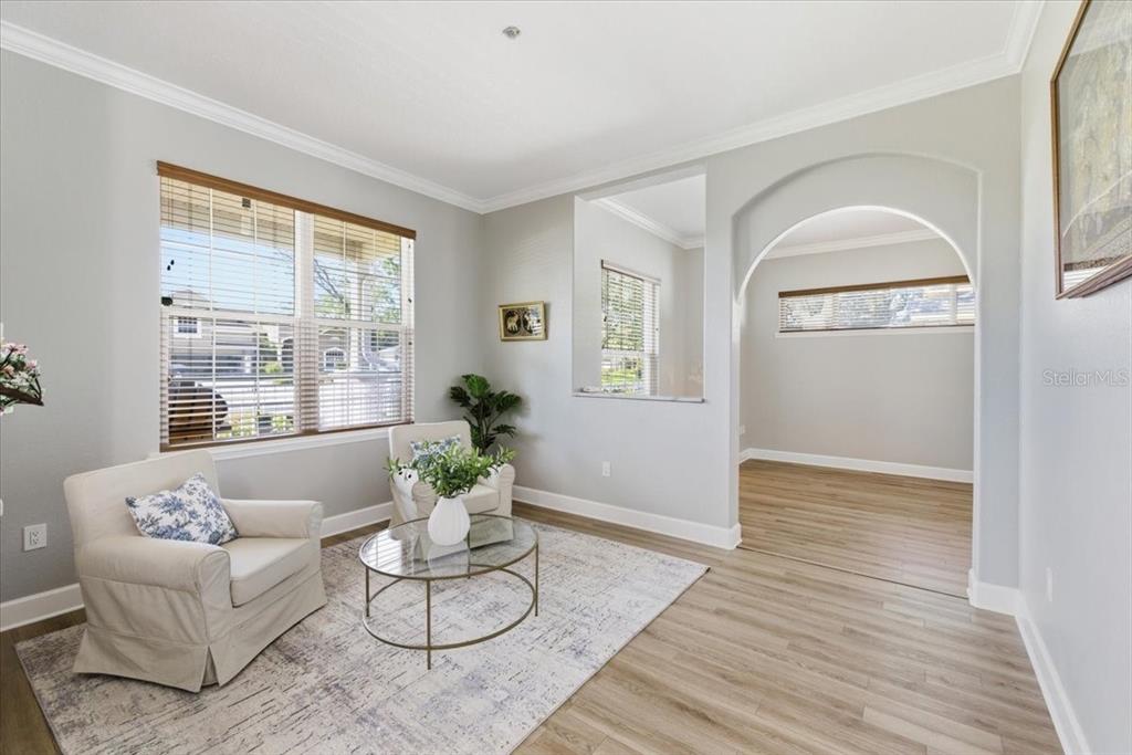 A living room features light gray walls, wood-look flooring, an arched entryway, and two armchairs — 2818 SHIPSTON AVENUE, NEW PORT RICHEY, FL