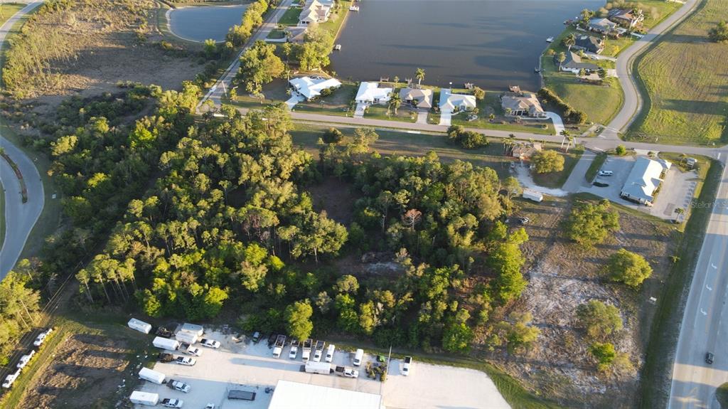 An aerial view shows a wooded lot situated between a road, a lake, and buildings — 12354 SW CO ROAD 769, LAKE SUZY, FL
