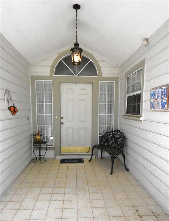 A covered porch features a white front door, side windows, a metal bench, and tile flooring — 12314 NW 8TH PLACE, NEWBERRY, FL