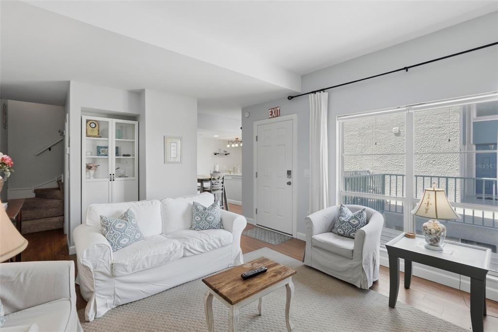 A living room features a white sofa, armchair, coffee table, and a door with an exit sign — 175 MEDALLION BOULEVARD UNIT F, MADEIRA BEACH, FL