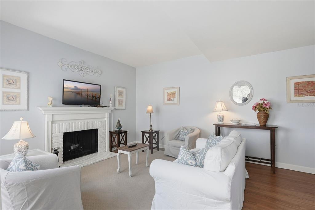 A living room features a white brick fireplace, light-colored walls, and white slipcovered furniture — 175 MEDALLION BOULEVARD UNIT F, MADEIRA BEACH, FL