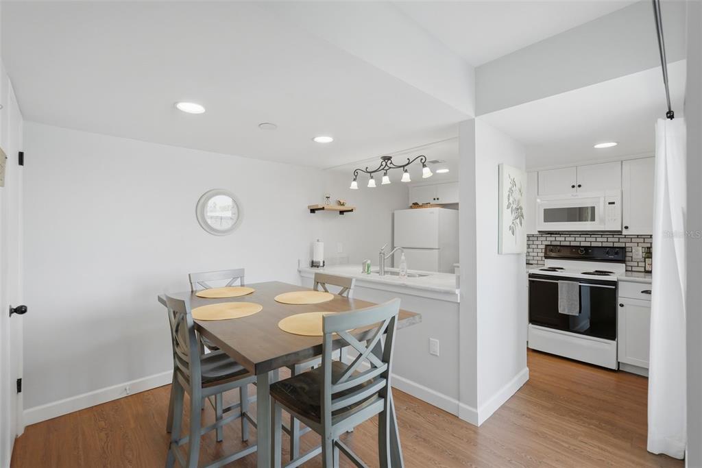A dining area with a wooden table and grey chairs adjacent to a white kitchen — 175 MEDALLION BOULEVARD UNIT F, MADEIRA BEACH, FL