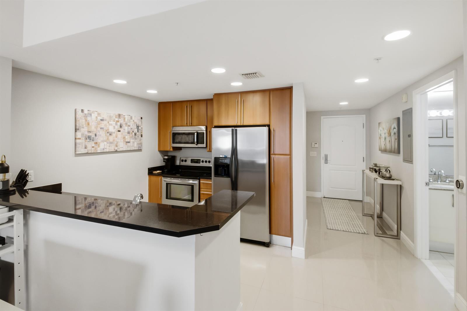 A kitchen with wood cabinets, stainless steel appliances, and a black countertop breakfast bar — 191 SE 20th Avenue # 210, Deerfield Beach FL 33441, DEERFIELD BEACH, FL