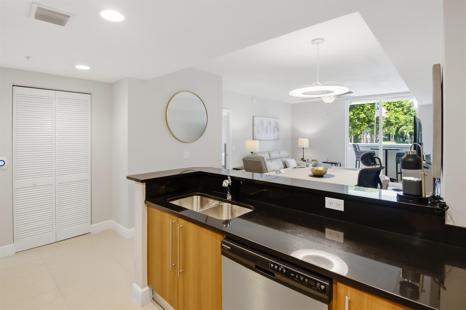 A kitchen with black countertops and wood cabinets overlooks a living area with a balcony — 191 SE 20th Avenue # 210, Deerfield Beach FL 33441, DEERFIELD BEACH, FL