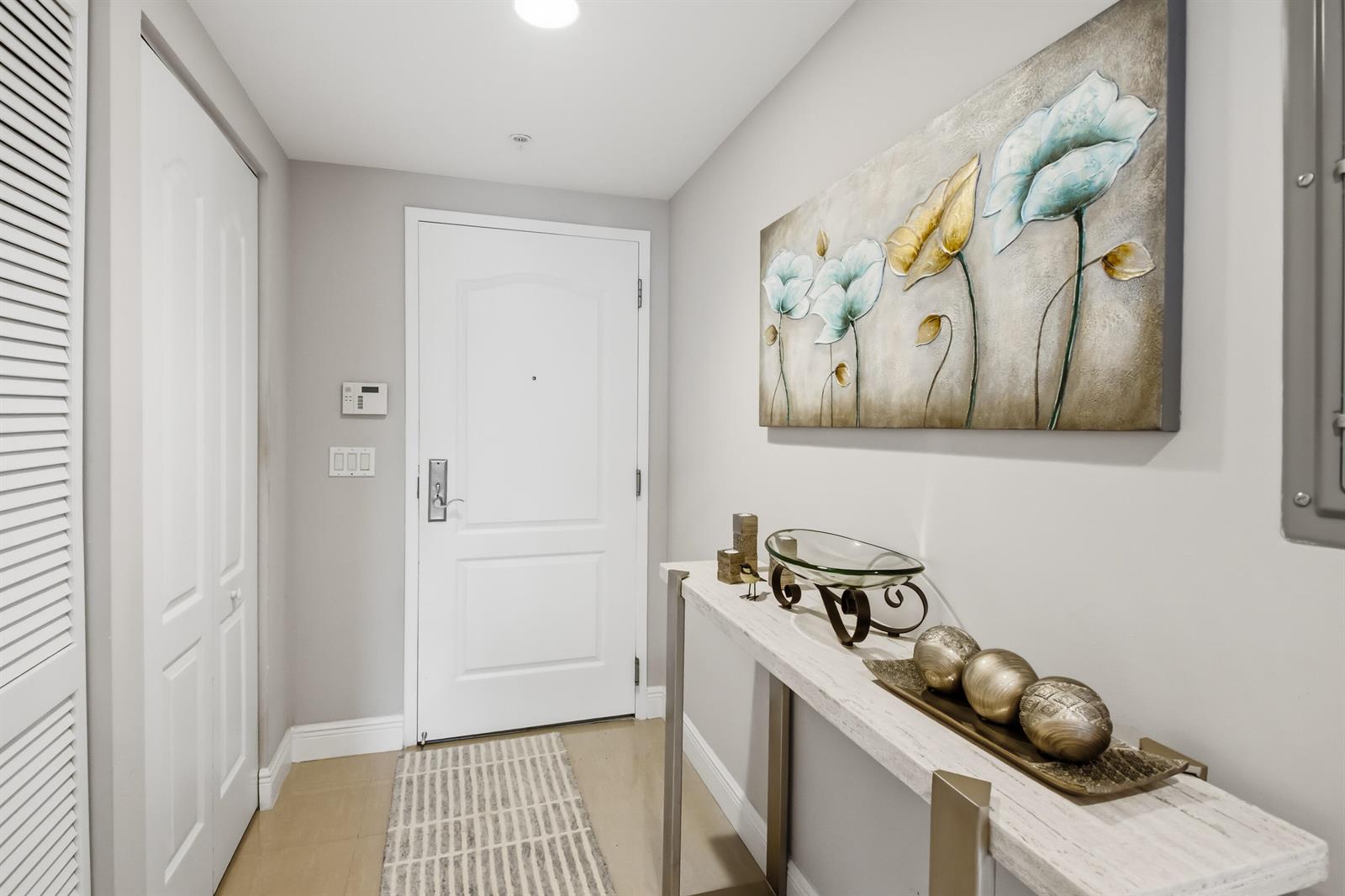 A bright entryway features a white door, a console table, and floral wall art — 191 SE 20th Avenue # 210, Deerfield Beach FL 33441, DEERFIELD BEACH, FL