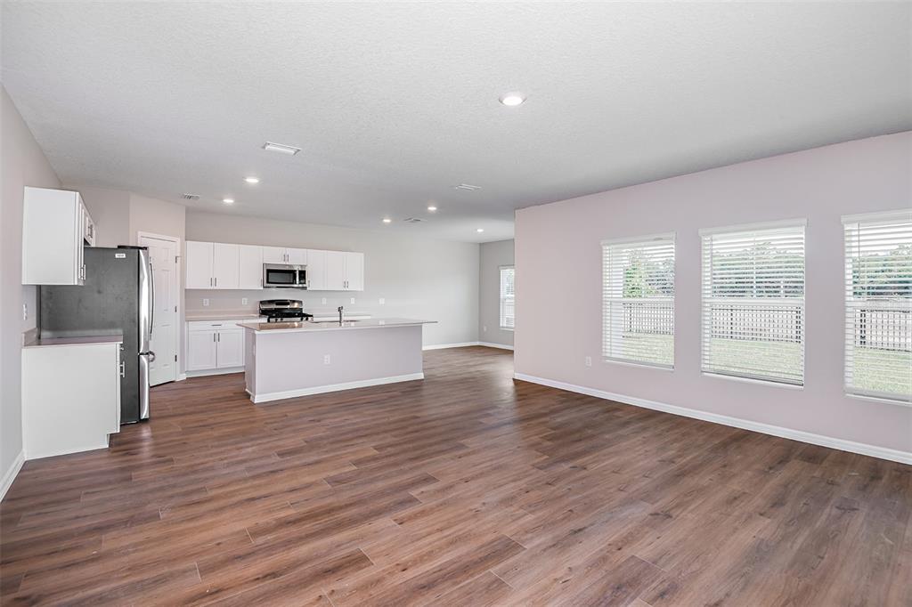 An open-concept kitchen and living area with white cabinets, stainless steel appliances, and wood flooring — 33647 NOBLE CREEK PLACE, DADE CITY, FL