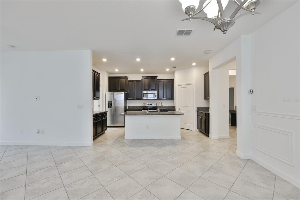 A kitchen features dark wood cabinets, granite countertops, a central island, and light tile flooring — 10616 GREAT CORMORANT DRIVE, RIVERVIEW, FL