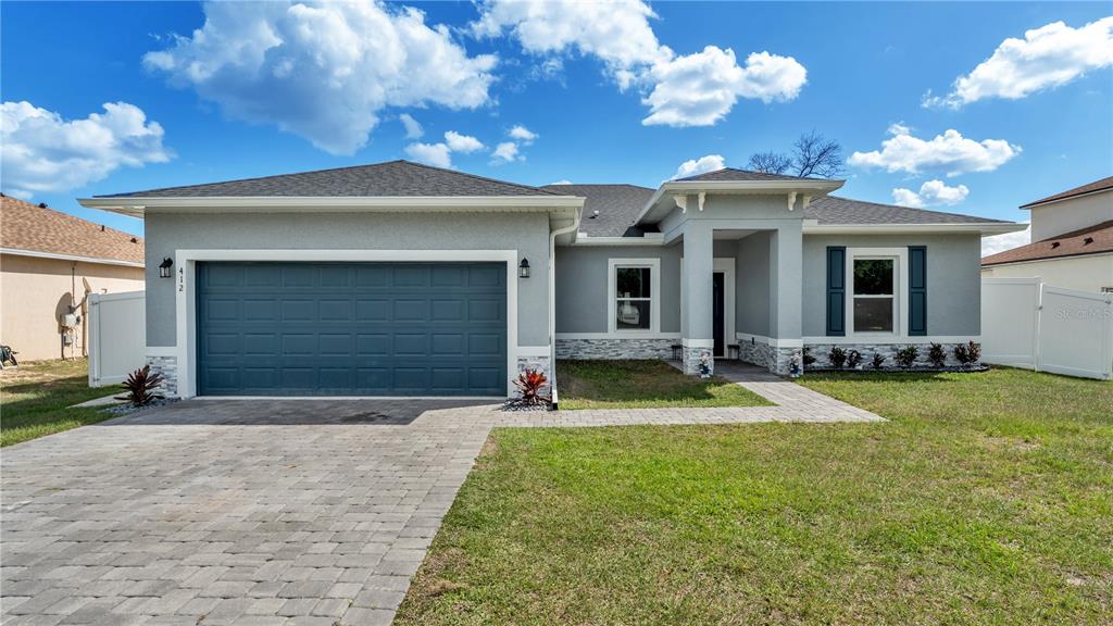A single-story house with a gray stucco exterior, stone accents, and a two-car garage — 412 ARKANSAS COURT, KISSIMMEE, FL