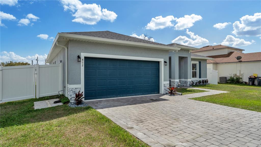A single-story house with a blue garage door, gray stucco siding, and a paver driveway — 412 ARKANSAS COURT, KISSIMMEE, FL