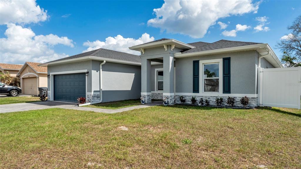 A single-story gray house with a two-car garage, stone accents, and a white privacy fence — 412 ARKANSAS COURT, KISSIMMEE, FL
