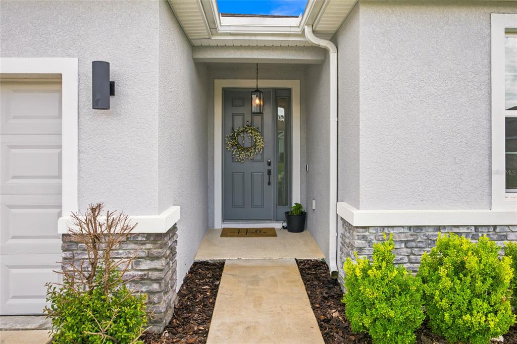 A gray front door with a wreath and a concrete walkway leading to the entrance — 1581 NE 50TH TERRACE, OCALA, FL