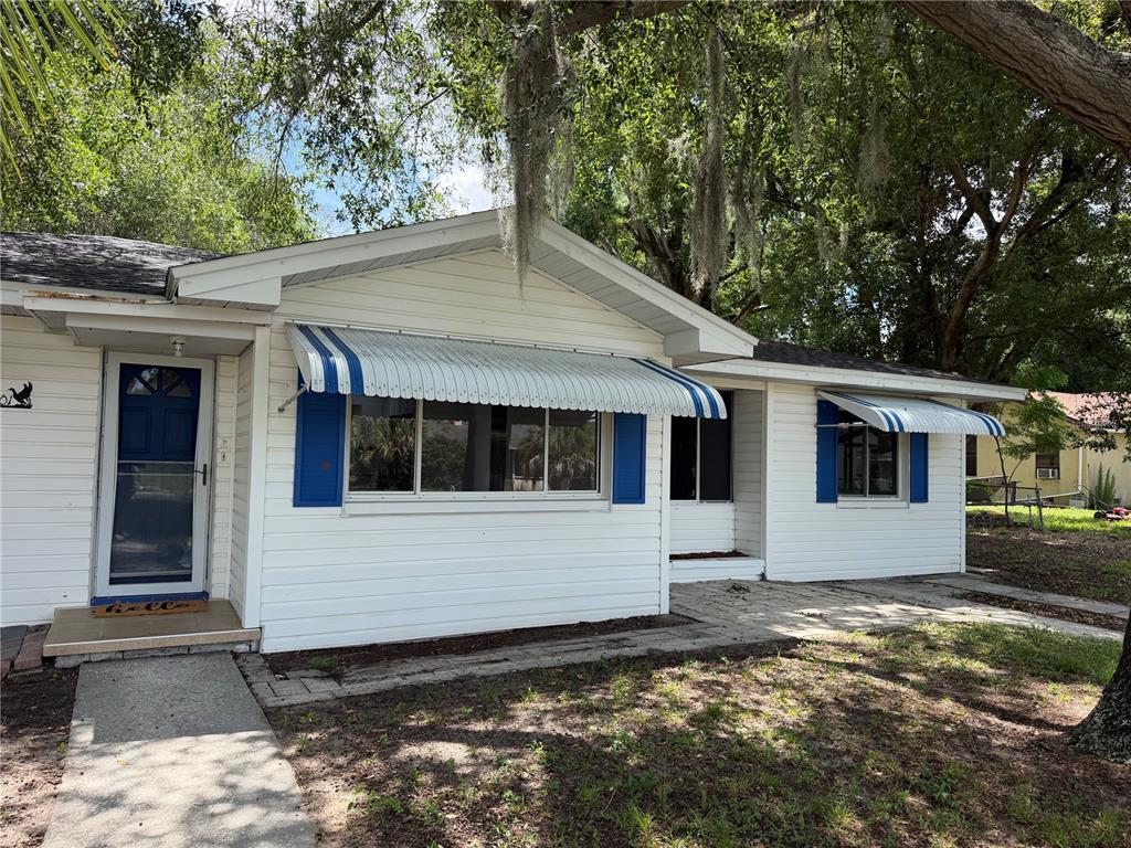 A white single-story house features blue window awnings, shutters, and a front entry door — 301 S SEMINOLE AVENUE, MINNEOLA, FL