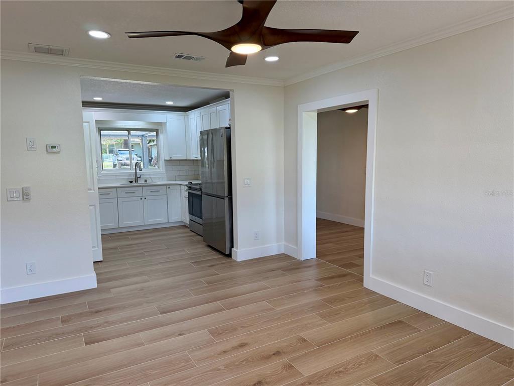 A room with light wood-look flooring leads to a kitchen featuring white cabinets and stainless appliances — 301 S SEMINOLE AVENUE, MINNEOLA, FL
