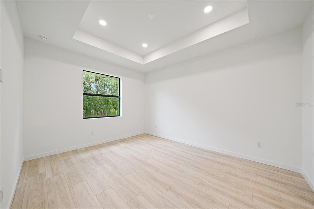 An empty bedroom features white walls, light wood-look flooring, and a recessed tray ceiling — 3938 ASCOT DRIVE, NORTH PORT, FL