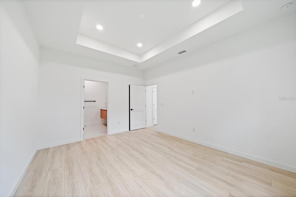 A minimalist bedroom features white walls, light wood-look flooring, and a recessed tray ceiling — 3938 ASCOT DRIVE, NORTH PORT, FL