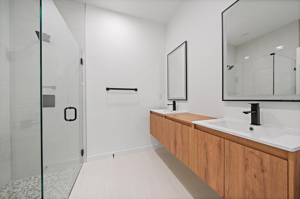 A modern bathroom features a double vanity with wood cabinets, black fixtures, and a glass shower — 3938 ASCOT DRIVE, NORTH PORT, FL