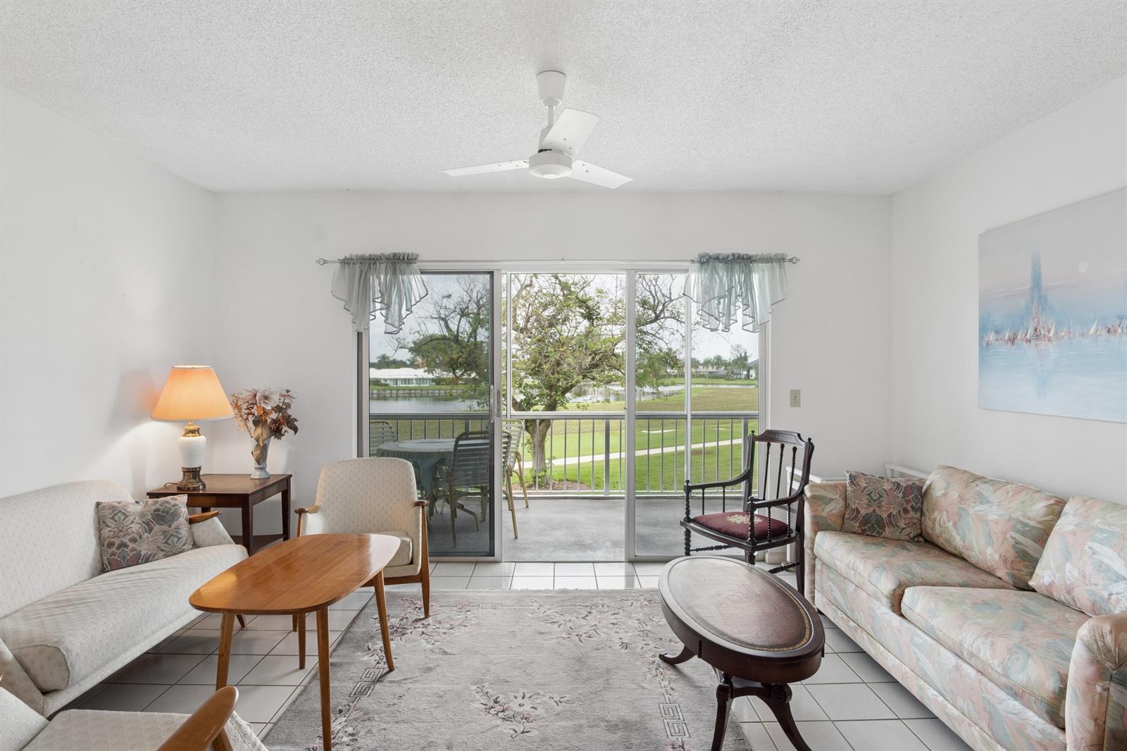 A living room with tile floors, two sofas, and sliding glass doors opening to a balcony — 250 John F Kennedy Drive # 202, Atlantis FL 33462, ATLANTIS, FL