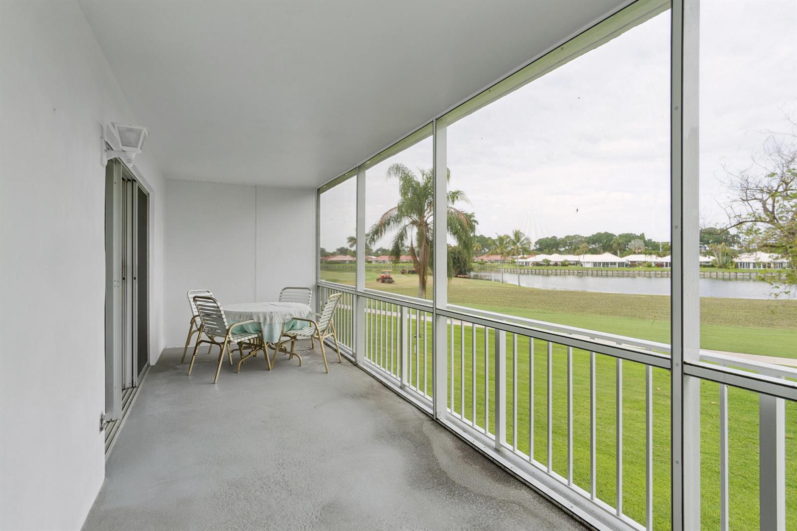 A screened-in balcony with a table, chairs, and a view of a lake and golf course — 250 John F Kennedy Drive # 202, Atlantis FL 33462, ATLANTIS, FL