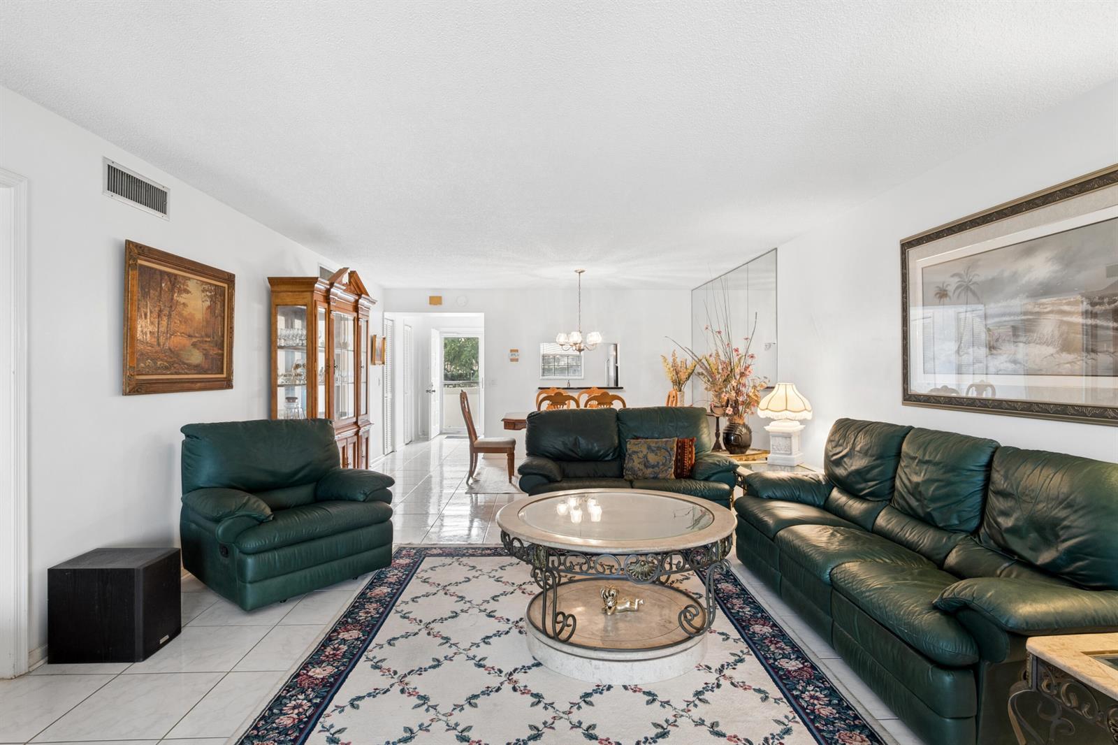 A living room with green leather furniture, a glass coffee table, and tile flooring — 250 John F Kennedy Drive # 202, Atlantis FL 33462, ATLANTIS, FL