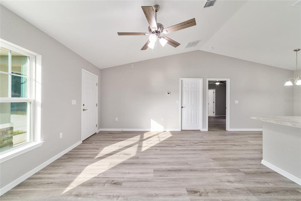 A living room with light gray walls, wood-look flooring, a ceiling fan, and two doors — 147 JUNIPER CIRCLE, OCALA, FL
