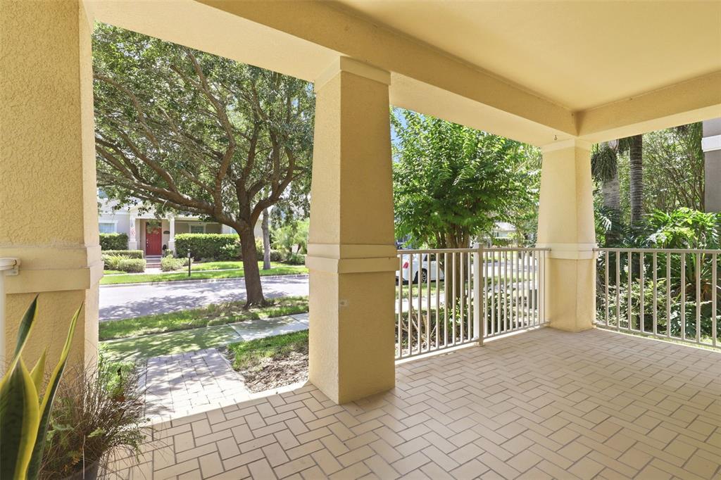 A covered porch with a herringbone-patterned tile floor, beige columns, and a white metal railing — 15621 SIGNATURE DRIVE, WINTER GARDEN, FL