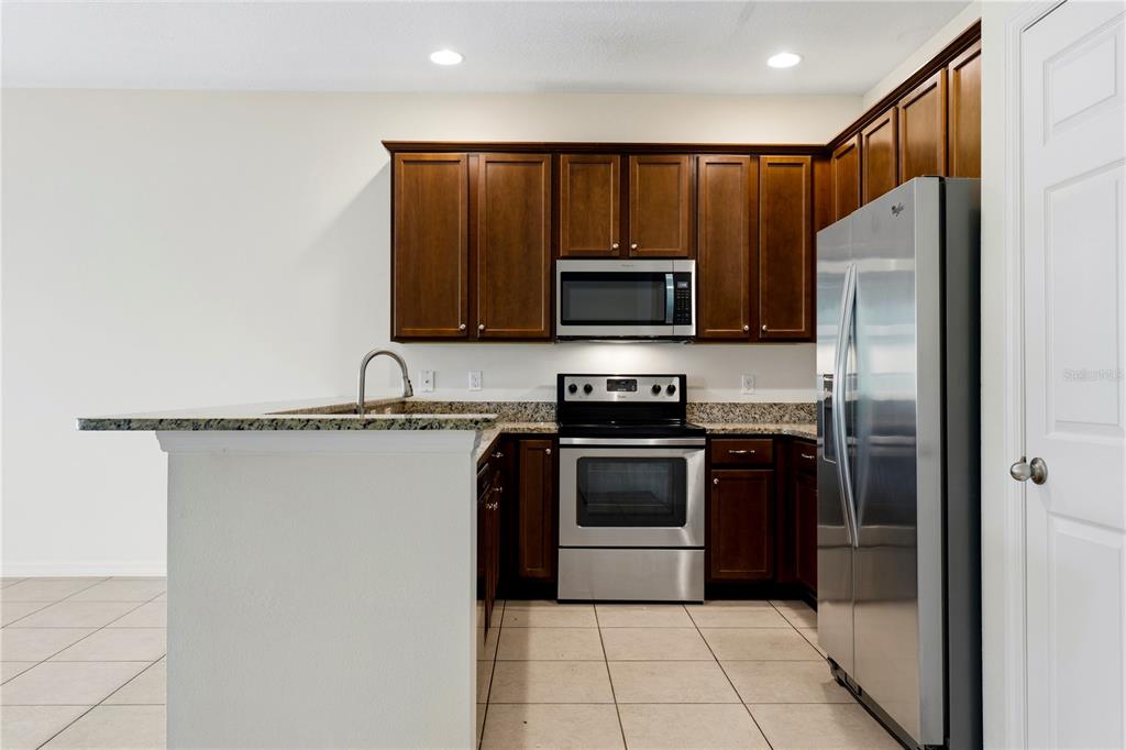 A kitchen features dark wood cabinets, stainless steel appliances, granite countertops, and tile flooring — 1253 HONEY BLOSSOM DRIVE, ORLANDO, FL