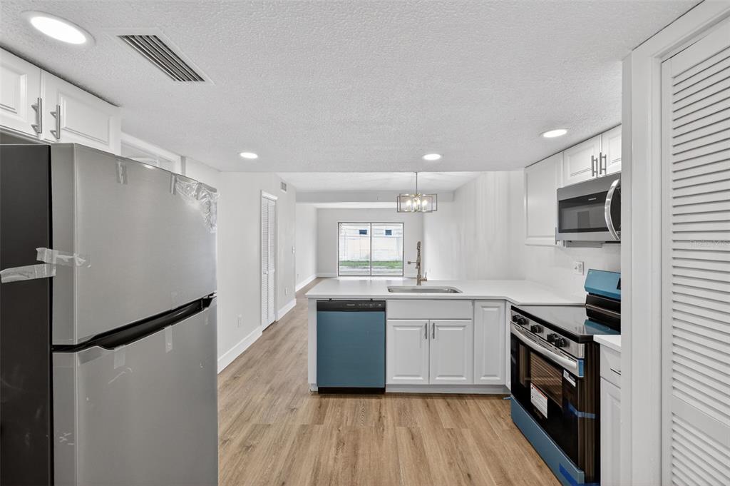 A kitchen with white cabinets, stainless steel appliances, and light wood-look flooring — 9824 POCONO STREET, PORT RICHEY, FL
