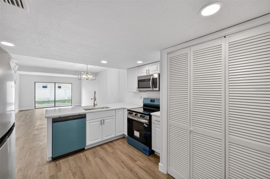 A kitchen with white cabinets, stainless steel appliances, and wood-look flooring opens to a living area — 9824 POCONO STREET, PORT RICHEY, FL