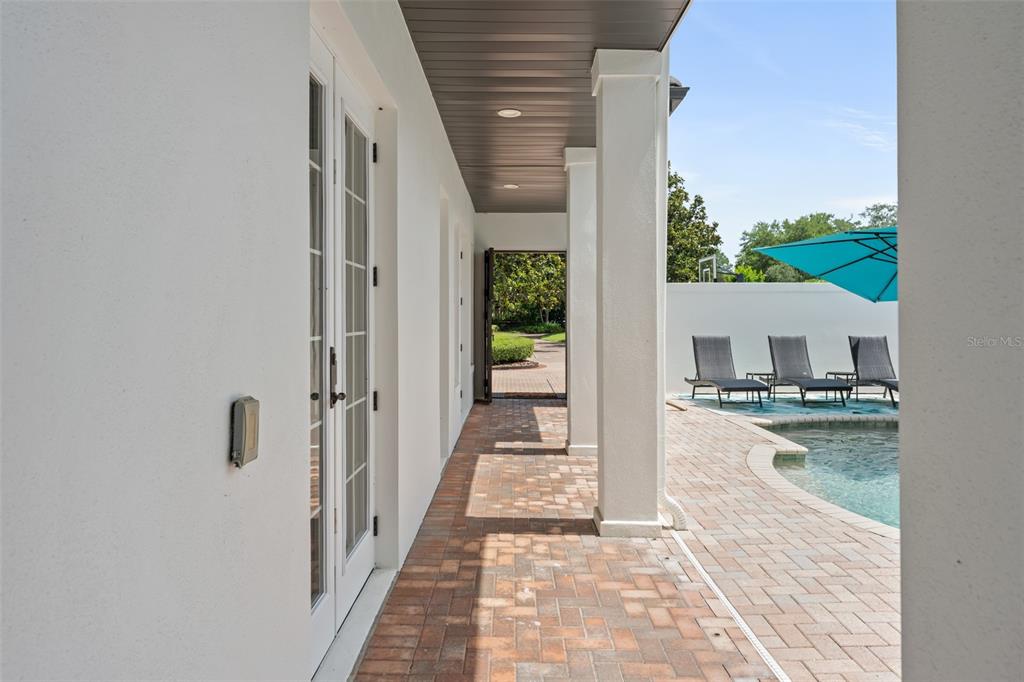 A covered brick patio overlooks a swimming pool with lounge chairs and a blue umbrella — 9720 COVENT GARDEN DRIVE, ORLANDO, FL