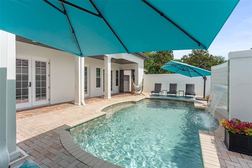 A backyard patio features a swimming pool with a water feature and two turquoise umbrellas — 9720 COVENT GARDEN DRIVE, ORLANDO, FL