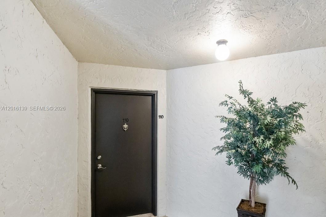 A black front door with the number 110 is situated in a white textured hallway — 825 Egret Cir # 110, Delray Beach FL 33444, DELRAY BEACH, FL