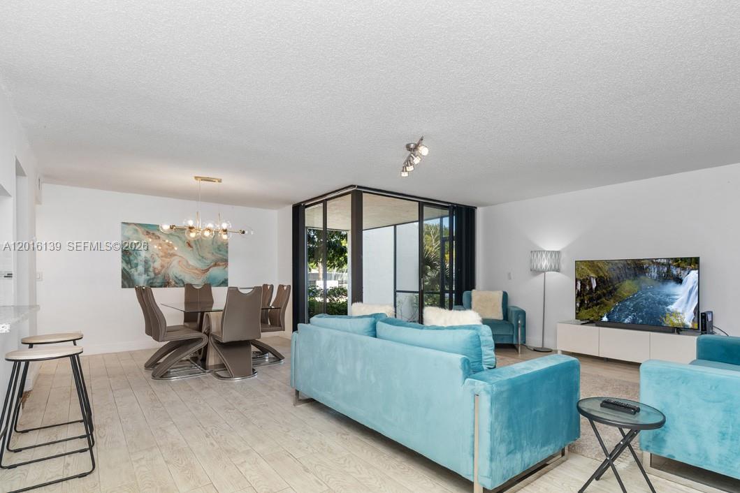 A living and dining area features light wood-look floors, blue velvet furniture, and a glass-enclosed patio — 825 Egret Cir # 110, Delray Beach FL 33444, DELRAY BEACH, FL