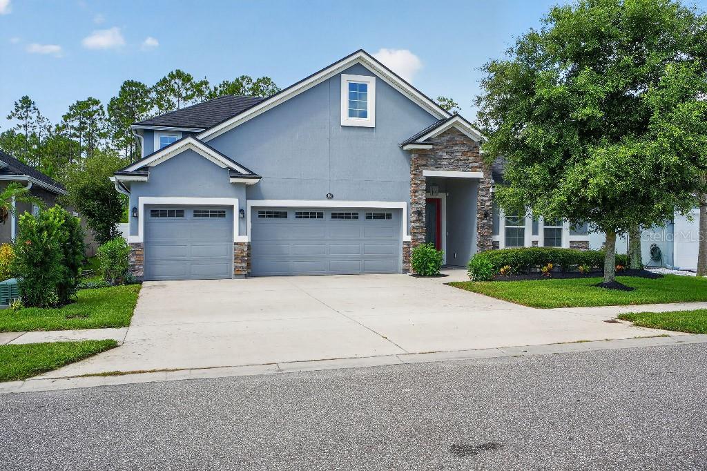 A two-story blue house with a three-car garage and stone accents on the front facade — 161 S COOPERS HAWK WAY, PALM COAST, FL