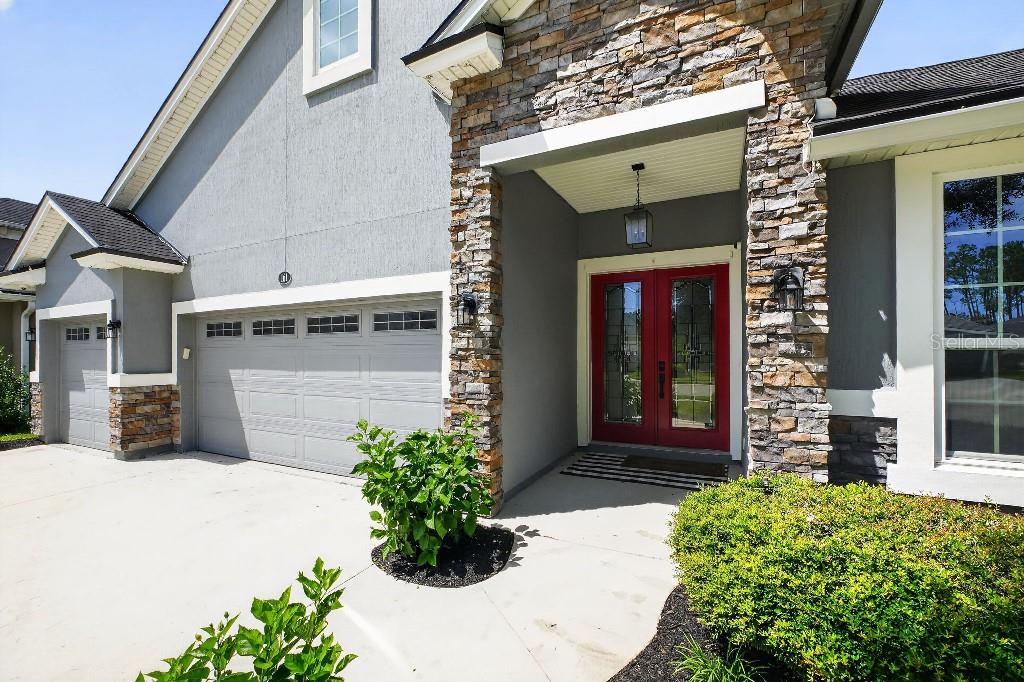 A house exterior featuring a red double front door, stone accents, and a gray garage — 161 S COOPERS HAWK WAY, PALM COAST, FL