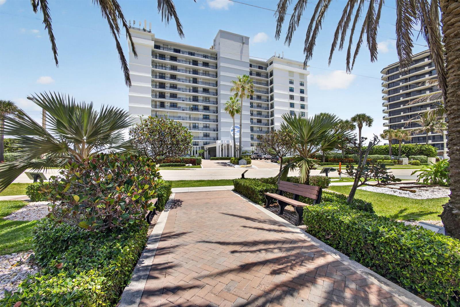 A paved walkway leads toward a multi-story white residential building surrounded by palm trees — 840 Ocean Drive # 406, Juno Beach FL 33408, JUNO BEACH, FL