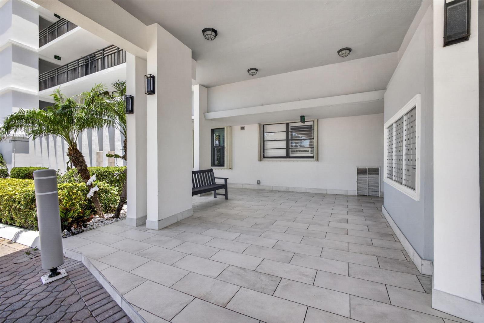 A covered outdoor patio features light-colored tile flooring, a dark bench, and wall-mounted mailboxes — 840 Ocean Drive # 406, Juno Beach FL 33408, JUNO BEACH, FL