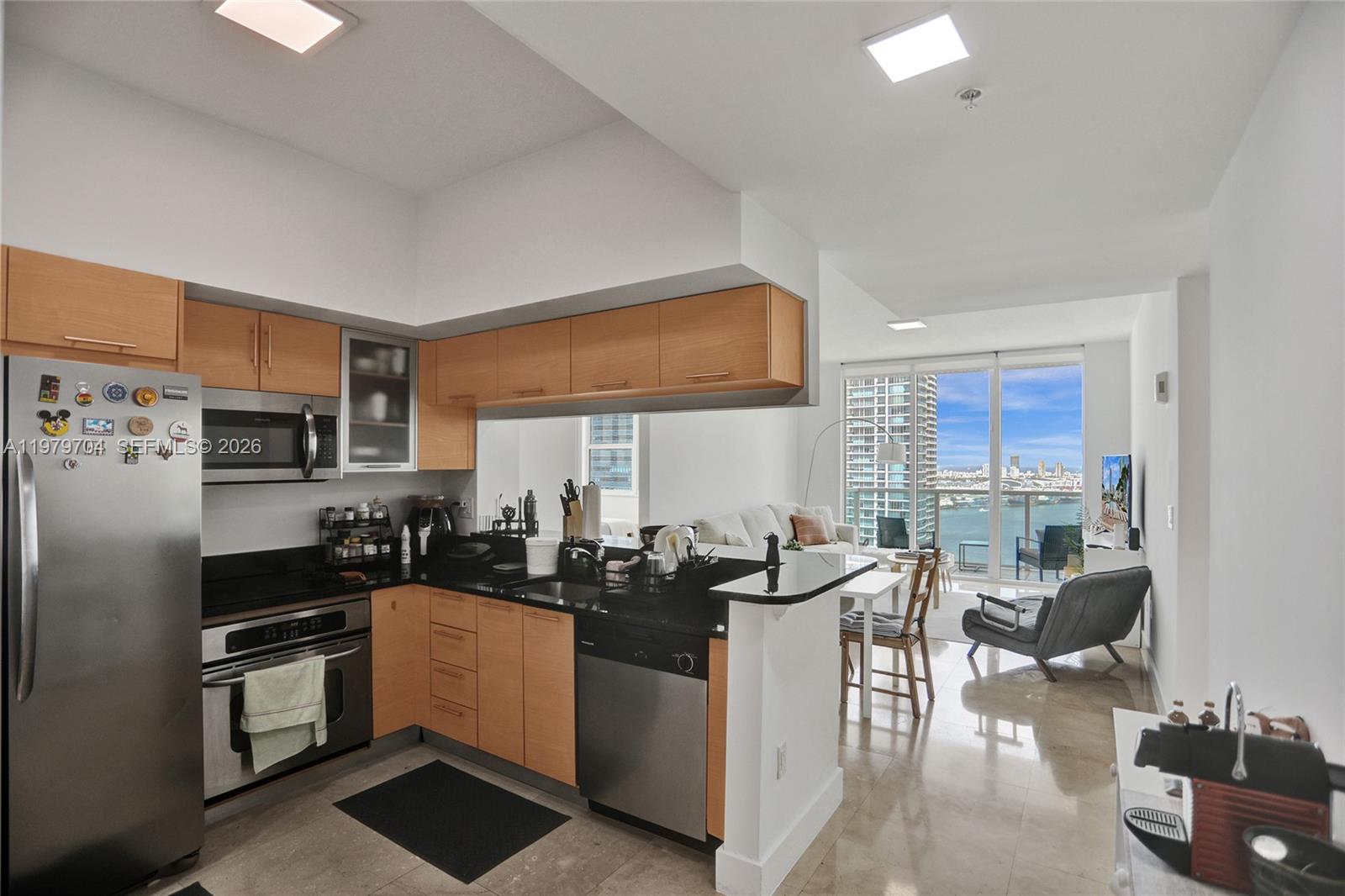 A kitchen with light wood cabinets and black countertops opens to a living area with views — 31 SE 5th St # 4112, Miami FL 33131, MIAMI, FL
