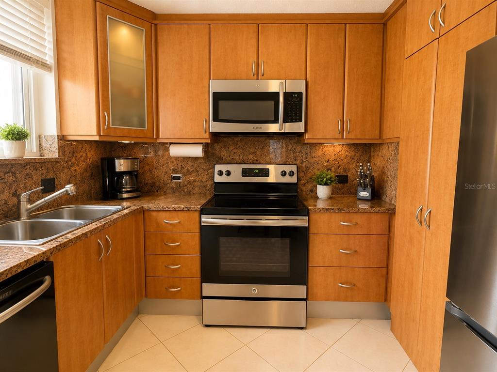 A kitchen features wood cabinets, granite countertops, stainless steel appliances, and light-colored tile flooring — 1035 ASHFORD AVE UNIT 802, SAN JUAN, PR