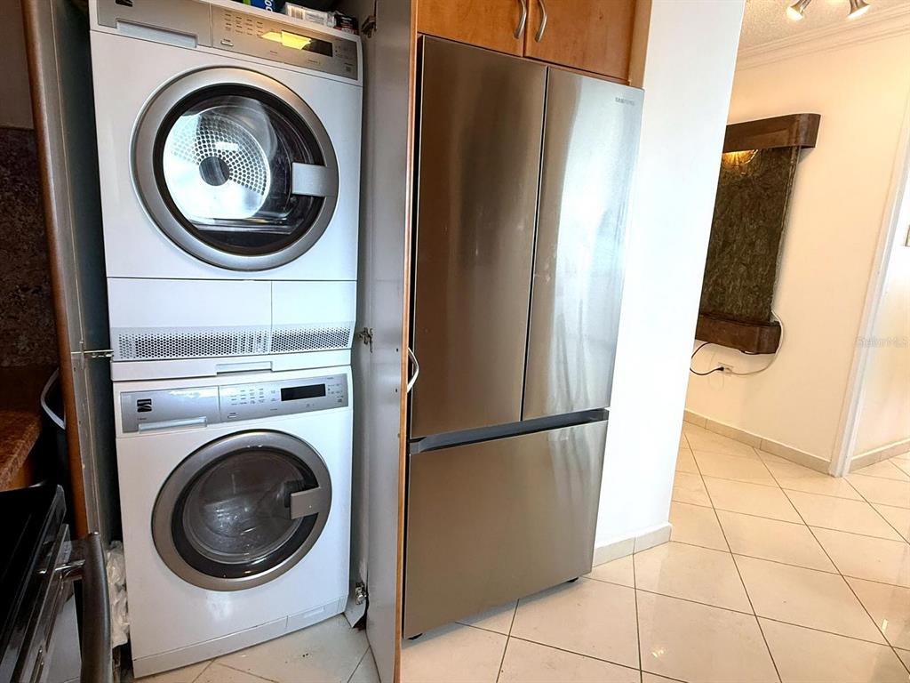 A stacked washer and dryer unit sits next to a stainless steel refrigerator in a kitchen — 1035 ASHFORD AVE UNIT 802, SAN JUAN, PR