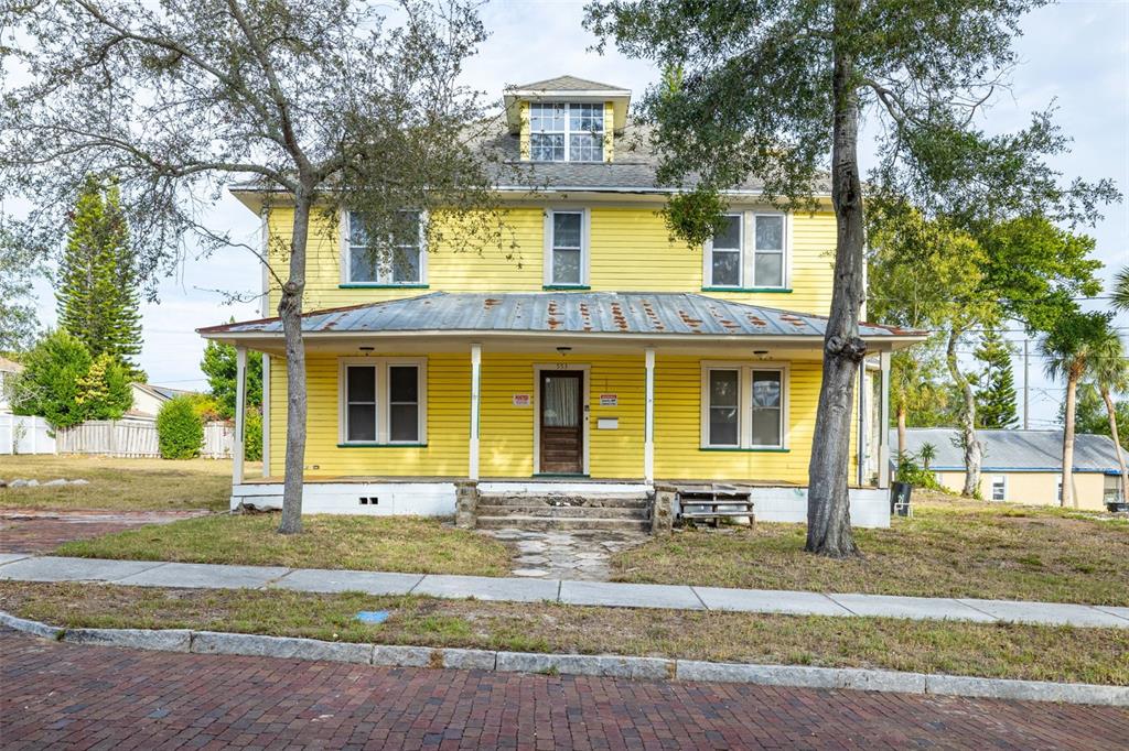 A two-story yellow house with a metal-roofed front porch stands behind a brick street — 553 DIVISION STREET, TARPON SPRINGS, FL