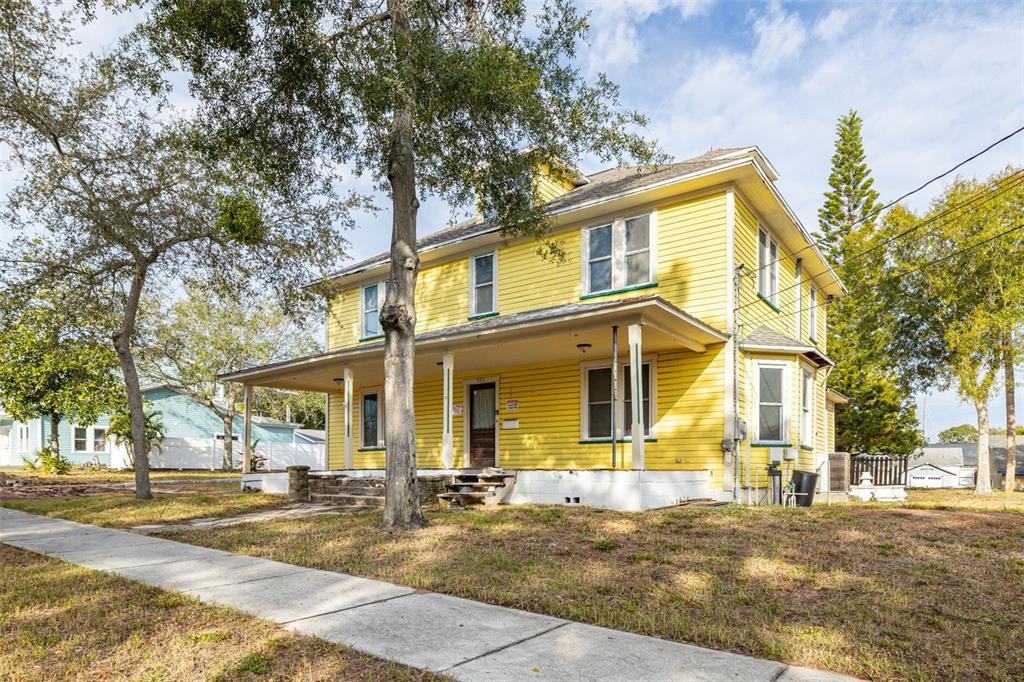 A two-story yellow house with a wrap-around porch stands on a grassy lot — 553 DIVISION STREET, TARPON SPRINGS, FL