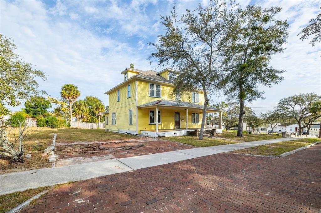 A yellow two-story house with a front porch sits behind a brick-paved street — 553 DIVISION STREET, TARPON SPRINGS, FL