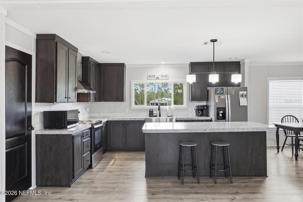 A kitchen features dark wood cabinets, a large island with bar seating, and light countertops — 2626 WILL ELLEDGE ROAD, GLEN ST MARY, FL