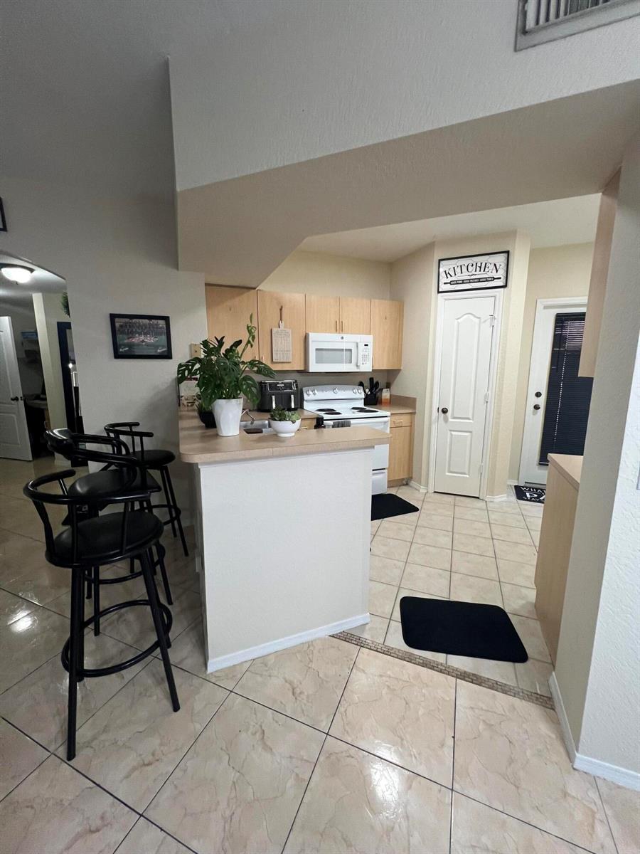 A kitchen features light wood cabinets, a breakfast bar with stools, and tiled flooring — 607 Belmont Place, Boynton Beach FL 33436, BOYNTON BEACH, FL