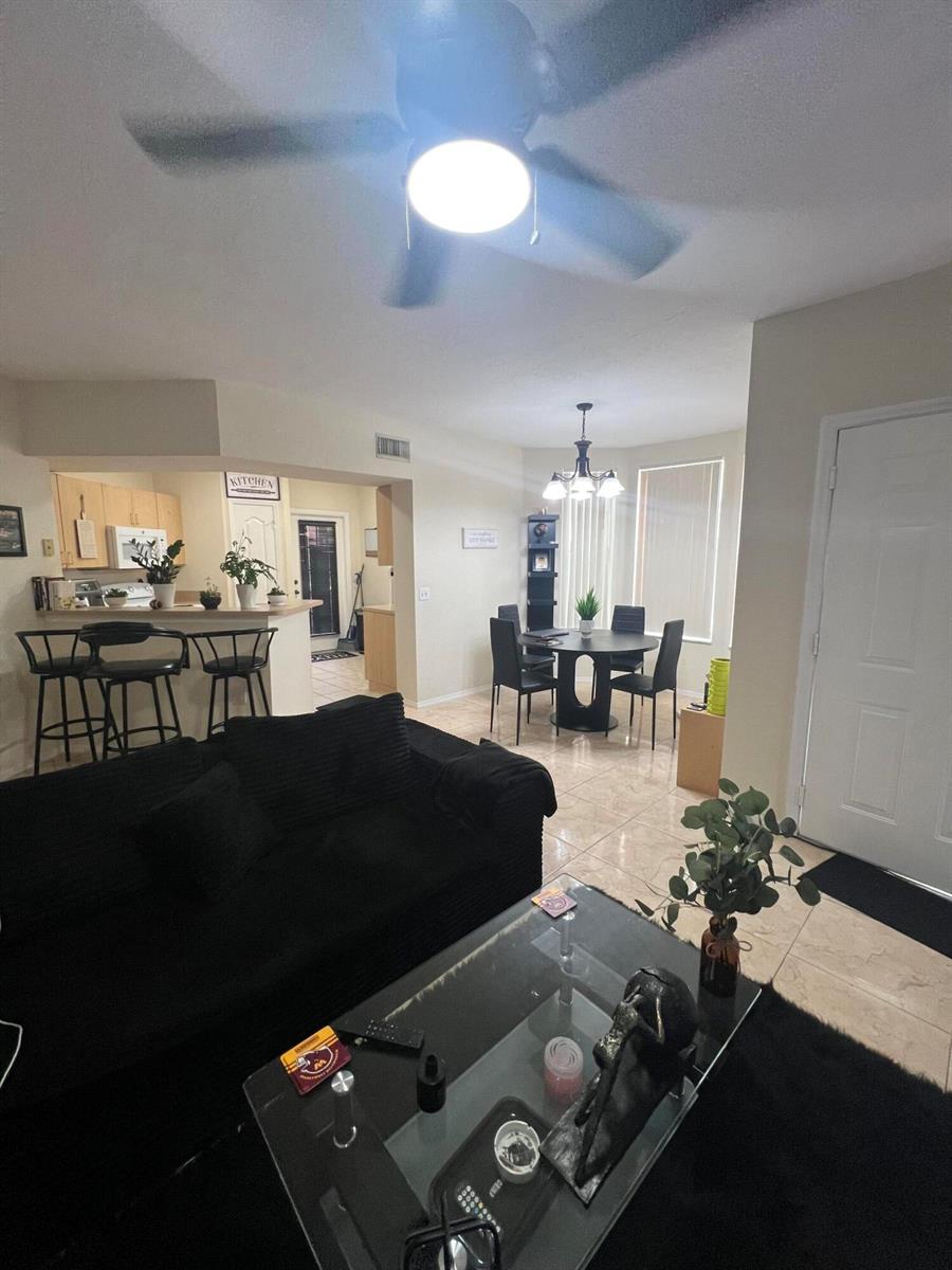 An open-concept living and dining area features tile flooring, a black sofa, and kitchen bar — 607 Belmont Place, Boynton Beach FL 33436, BOYNTON BEACH, FL