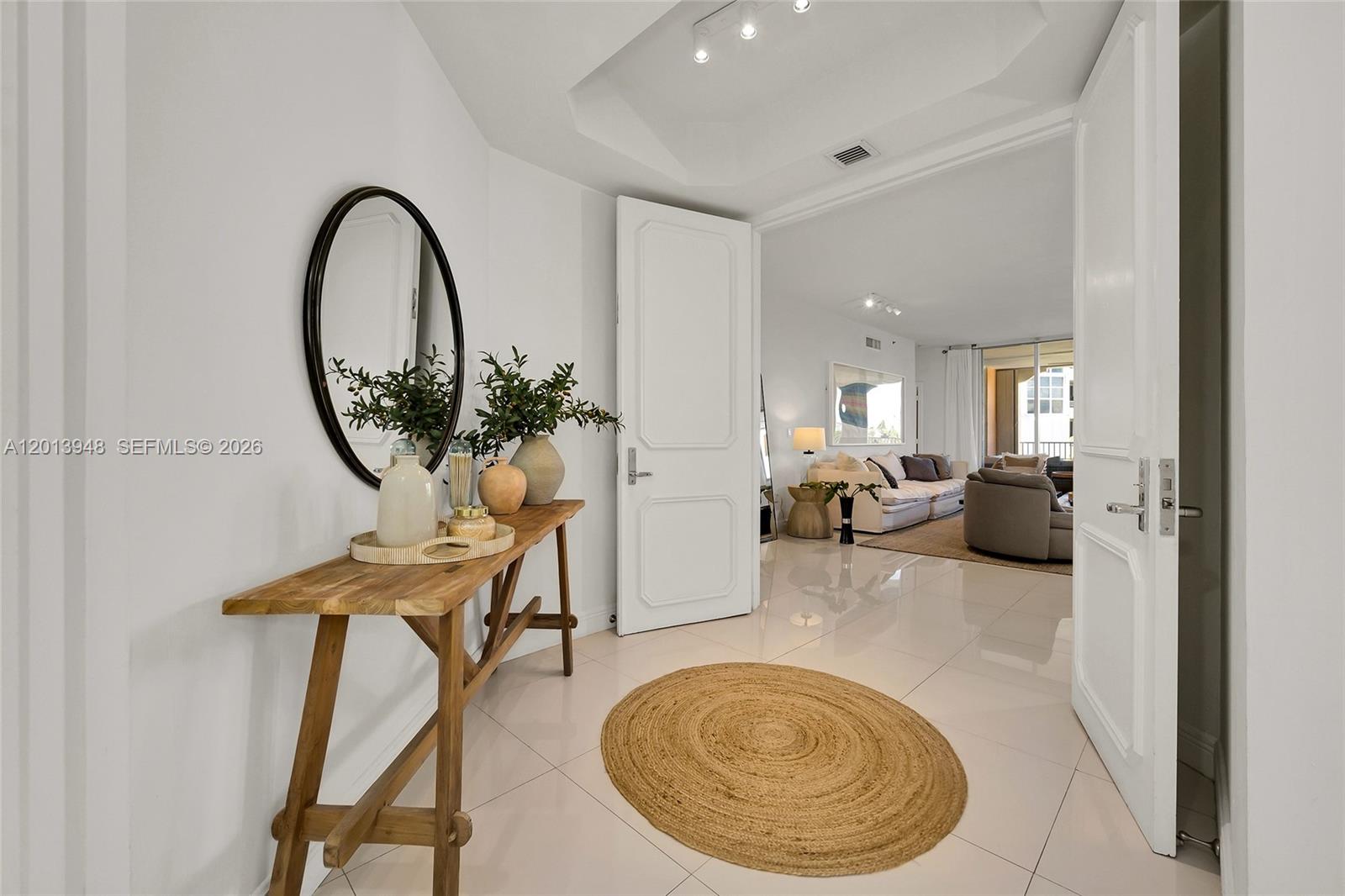 A bright entryway features a wooden console table, a round mirror, and a jute rug — 733 Crandon Blvd # 406, Key Biscayne FL 33149, KEY BISCAYNE, FL