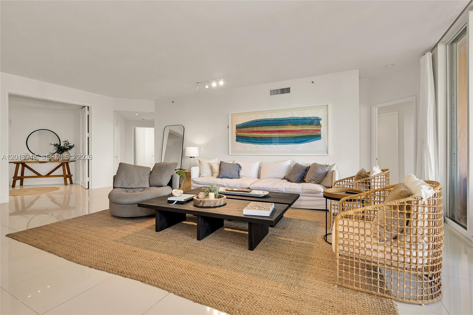 A bright living room features a white sofa, dark coffee tables, and woven armchairs — 733 Crandon Blvd # 406, Key Biscayne FL 33149, KEY BISCAYNE, FL