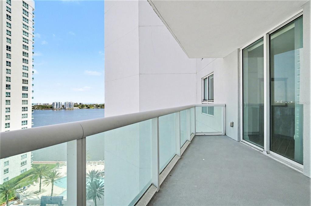 A balcony with a glass railing overlooks a body of water and nearby high-rise buildings — 231 RIVERSIDE DRIVE UNIT 1110, DAYTONA BEACH, FL